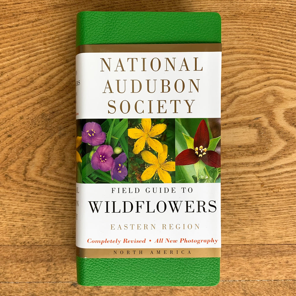 Field guide with bright green faux-leather cover and paper cover over it featuring flower photos and book title