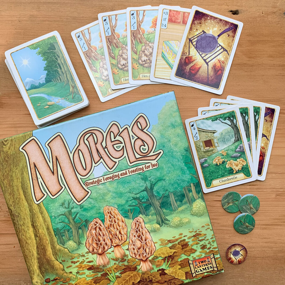 Morels board game box cover featuring illustration of morel mushrooms growing in a forest.  Also shown are several game cards and game pieces featuring illustrations of several other mushrooms and a cast iron on a grill over a campfire.