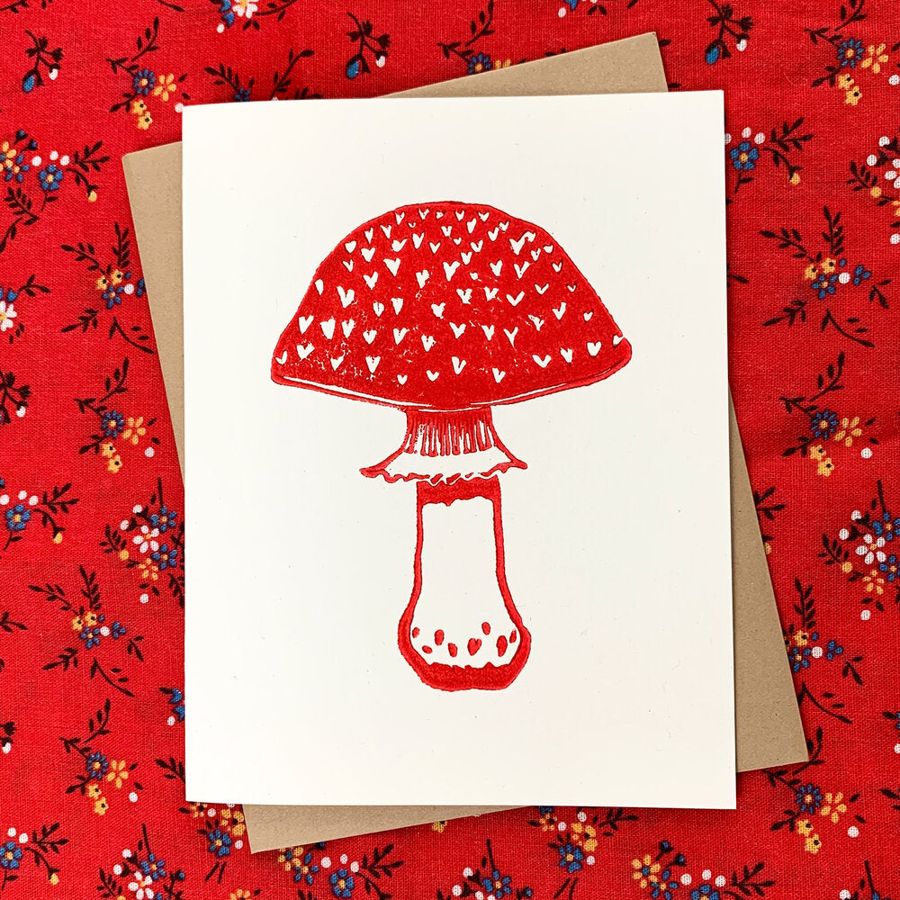 Block printed greeting card with bold red print of an amanita mushroom with hearts in place of the characteristic white warts of an amanita.