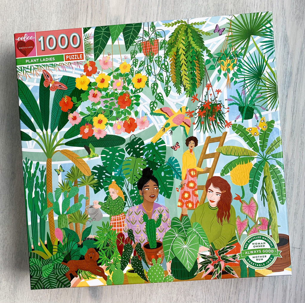 Front cover of jigsaw puzzle box displaying several women and a dog enjoying their time amongst many plants and flowers in a greenhouse.