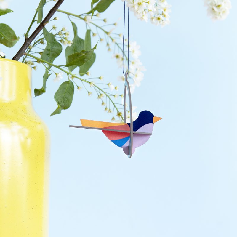Colorful cardboard three dimensional robin ornament hanging from a house plant.
