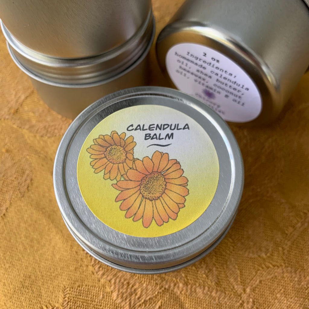 Metal tins of balm with orange calendula flowers on the label