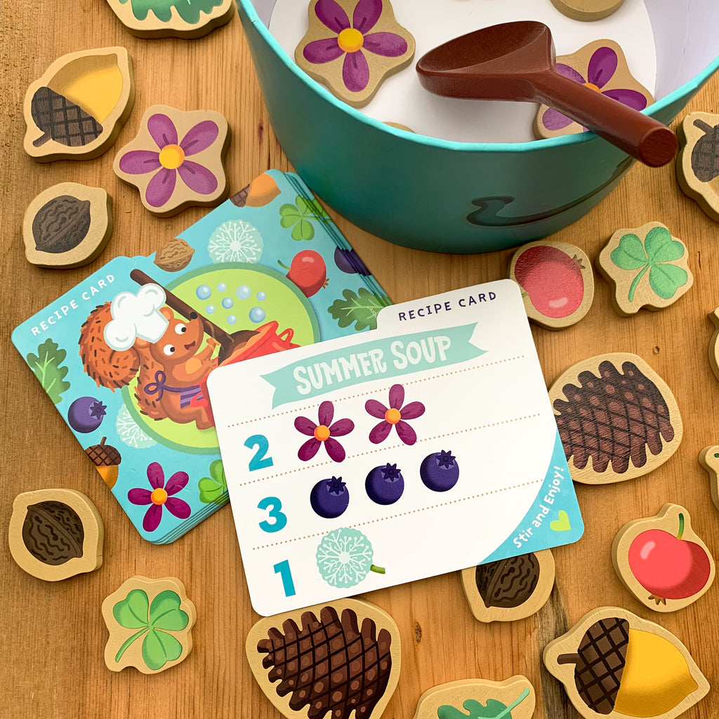 Game pieces including wooden tokens of pinecones, clover, flowers, acorns, etc. plus the game's "recipe cards," circular box and stirring spoon
