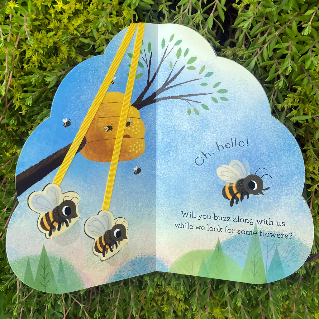 Hello Honeybees hive-shaped board book opened to first page showing hive shape of the book and two pop-out cartoon bees on yellow straps that can visit each page.