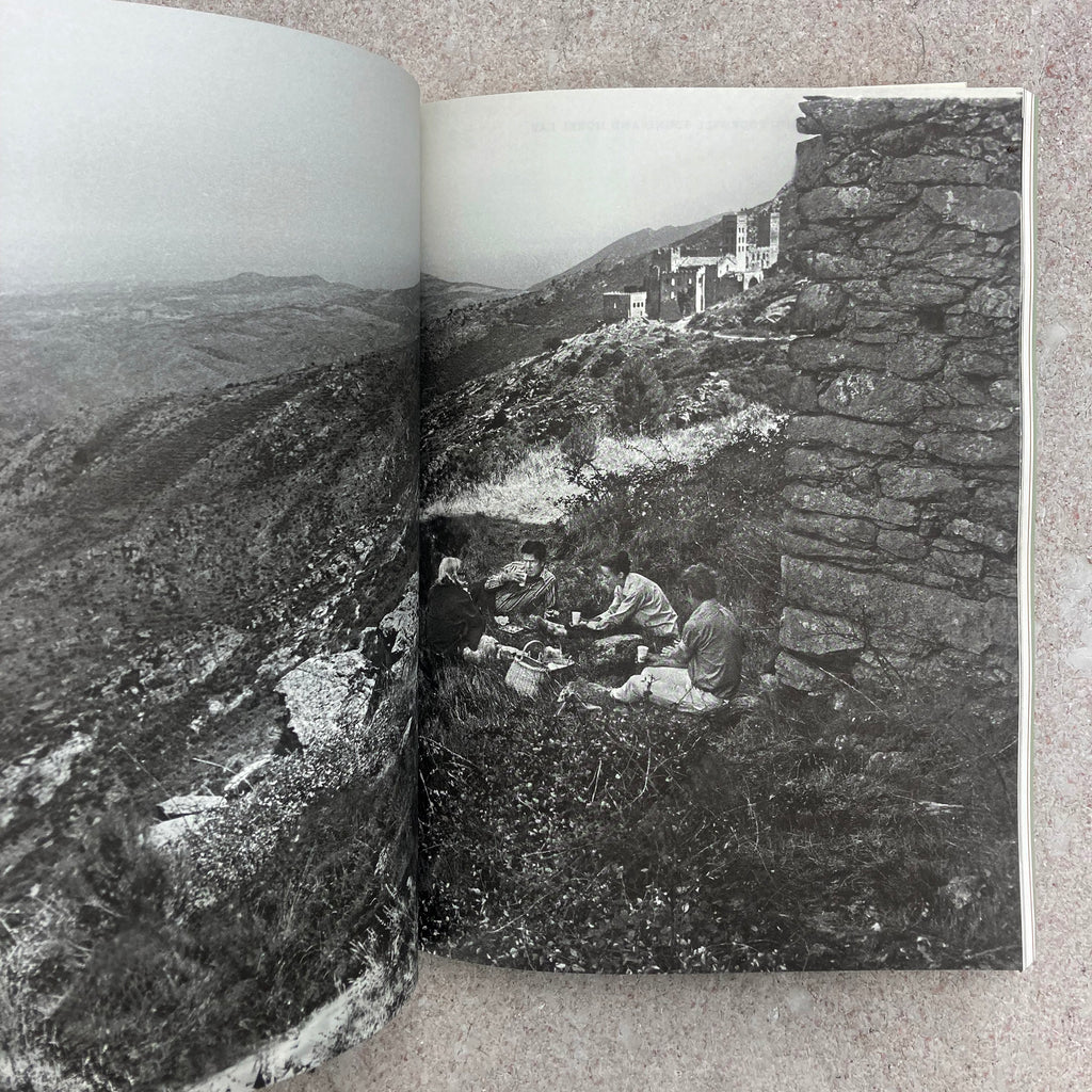 Photo of an inside page of A MYCOLOGICAL FORAY featuring a two page spread photograph of John Cage and company having a meal on a hillside next to a rustic-looking stone structure.
