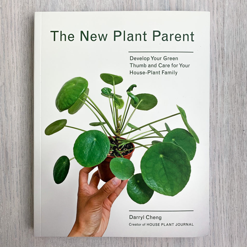 Paperback front cover of The New Plant Parent with a photograph of a hand holding up a house plant with giant leaves on thin stalks.
