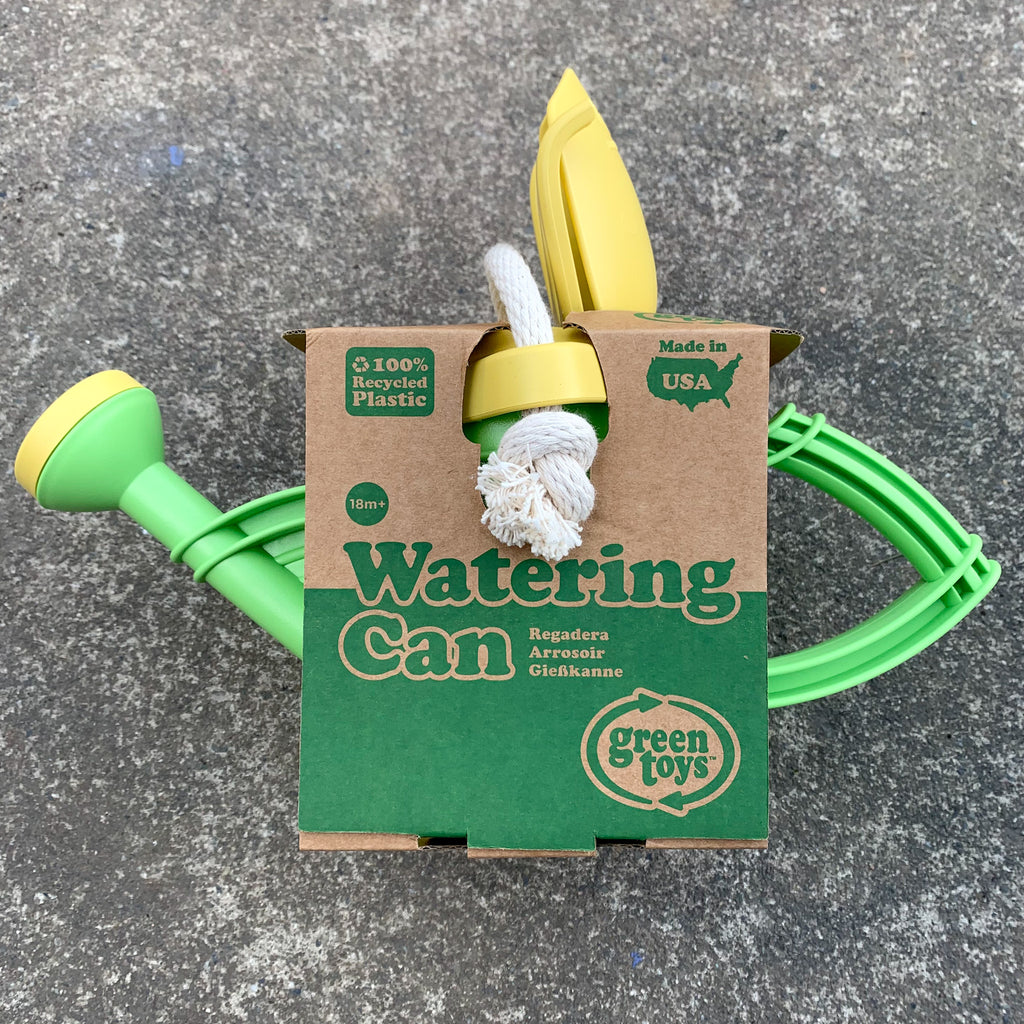 Green recycled plastic watering can with yellow accents in its cardboard packaging.