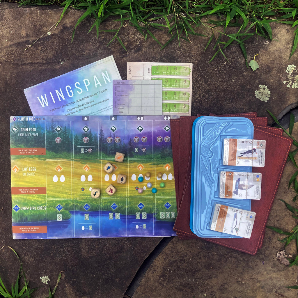 Contents of WINGSPAN game box including decks of bird cards, playing boards, dice, small colorful egg playing pieces, score cards, and instruction books.